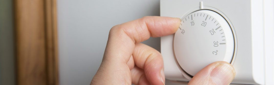 Hand adjusting the dial on an air conditioner thermostat.
