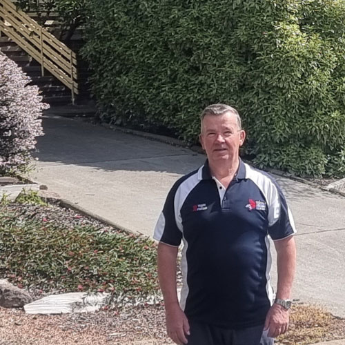 An image of Eugen standing outside his suburban Canberra home in a blue polo shirt.